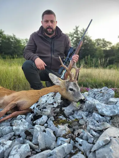 Un cacciatore con pile marrone accanto a un capriolo su calcare frantumato
