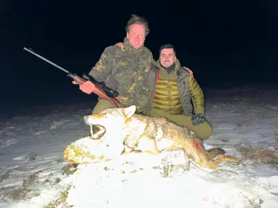 Due cacciatori seduti insieme nella neve di notte accanto a un lupo, sorridenti